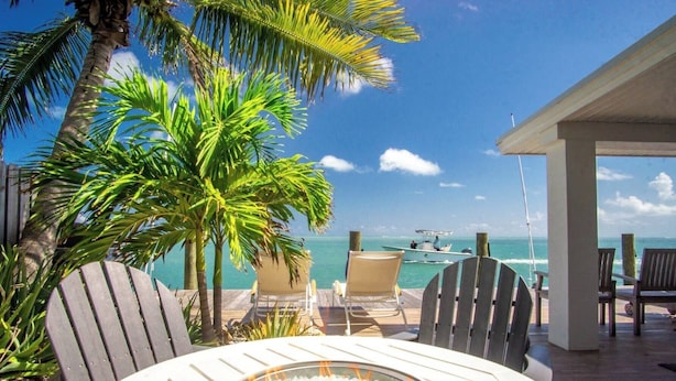 A deck with chairs overlooking a beach, a fire pit, and a view of the ocean. - Dolfan Oceanfront Cottage Direct oceanfront with 50 ft of dockage and jacuzzi and kayaks 4 bed 2 bath home (Marathon)