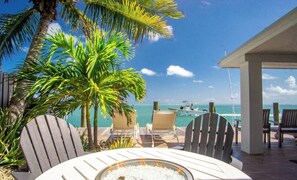 Een terras met stoelen met uitzicht op een strand, een vuurkuil en een uitzicht op de oceaan.