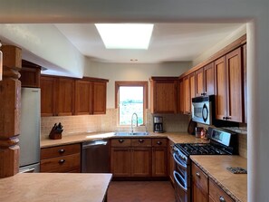 A kitchen with wooden cabinets, a dishwasher, a stove, and a microwave. - Truly Taos Garden in the Desert (El Prado)
