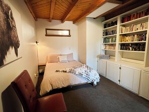 Un dormitorio con una cama, una estantería, una silla y una lámpara de pared.