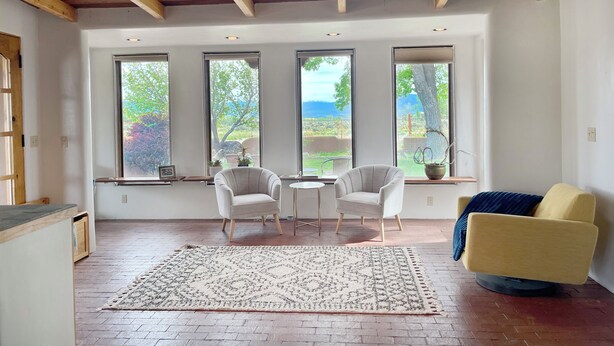 Une pièce spacieuse avec un plafond haut, de grandes fenêtres et un coin salon confortable comprenant deux fauteuils et un canapé.