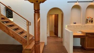 A wooden staircase leading to a hallway with a kitchen area, including a countertop and cabinets.