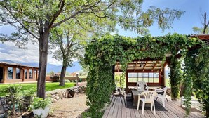 Une terrasse en bois avec des sièges extérieurs, entourée de verdure et d’un mur en pierre.
