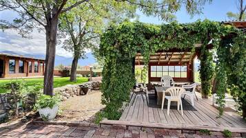 A wooden deck with outdoor seating, surrounded by greenery and a stone wall.