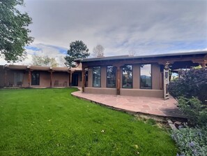 A house with a covered patio, a lawn, and a view of the mountains. - Truly Taos Garden in the Desert (El Prado)