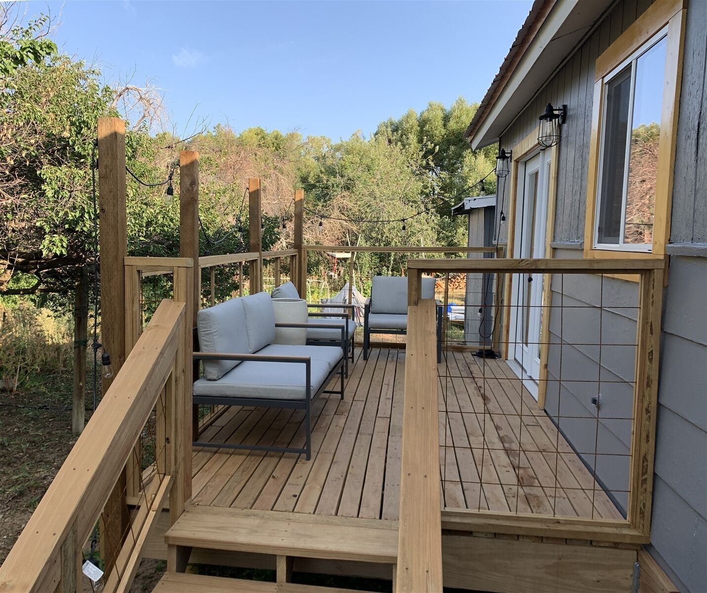 A wooden deck with outdoor seating, a small table, and a window with a view of trees.