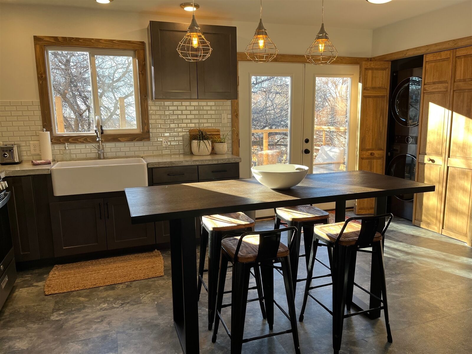 A modern kitchen with a central island, bar stools, pendant lighting, and a view through the windows.