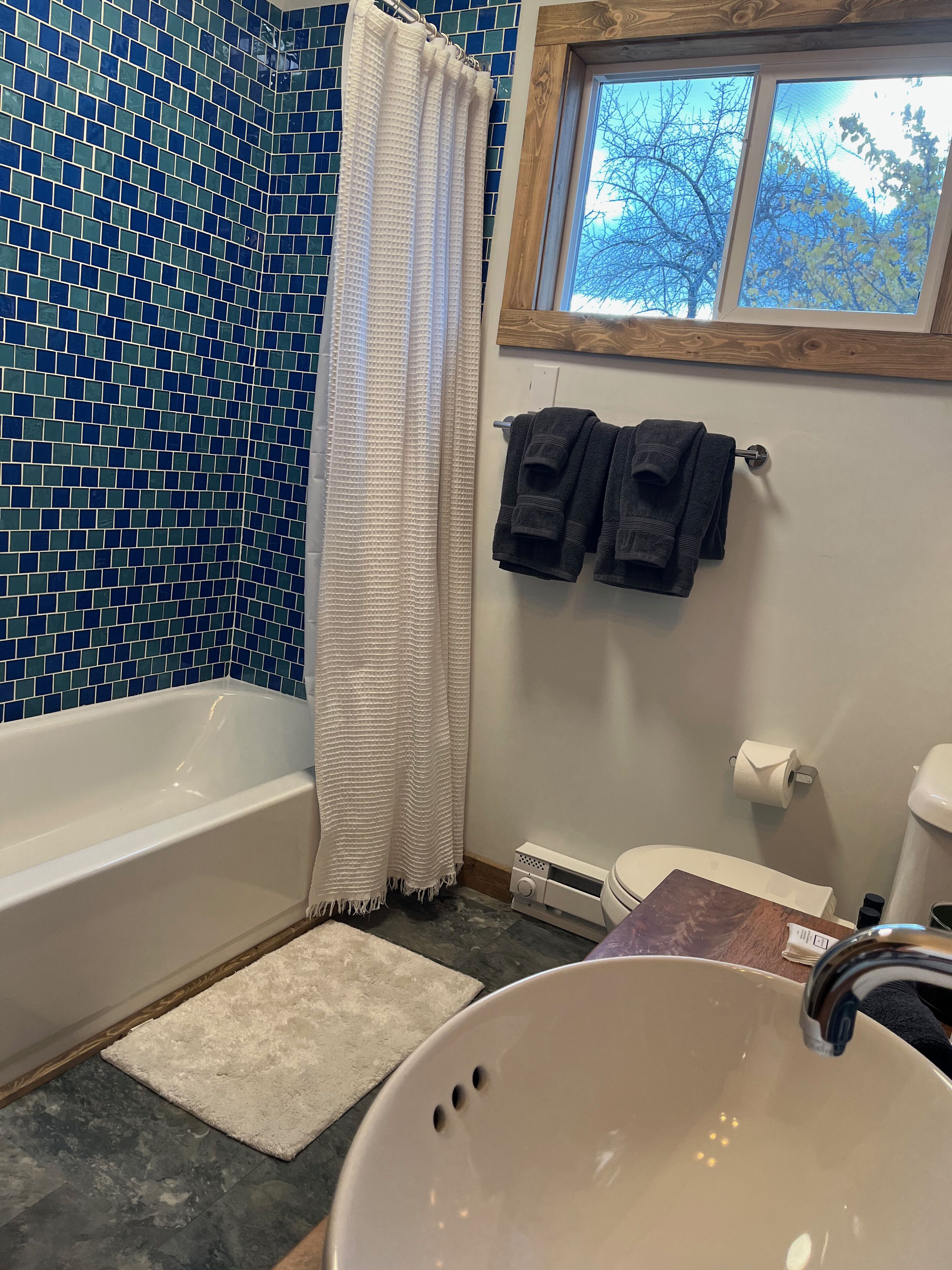 A bathroom with a bathtub, a sink, a toilet, a window with a view of trees, and a towel rack with towels.