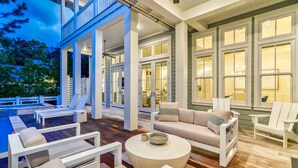 Una amplia terraza exterior con mobiliario blanco, una mesa redonda y un ventanal que da a una habitación.