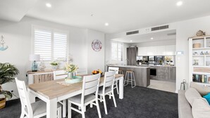 A modern kitchen with white cabinetry, a central island, and a dining area with a wooden table and white chairs.