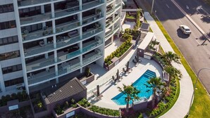 A high-rise building with a rooftop pool, outdoor seating, and a street view.
