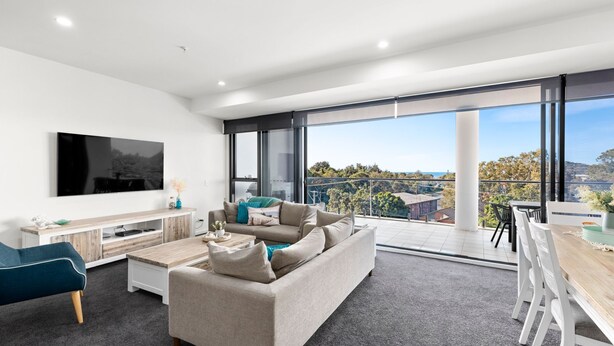 A modern living room with a large flat-screen TV, a sofa, and a dining area with a view of the city.