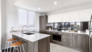 A modern kitchen with a central island, bar stools, a built-in oven, and a view of the outdoors through the window.