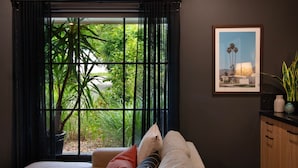A room with a large window, a sofa, a framed picture, and a plant on a cabinet. - East St 1 - tranquil escape, cosy charm (Daylesford)