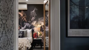 Een slaapkamer met een bed, nachtkastje, lamp en een lijst aan de muur.