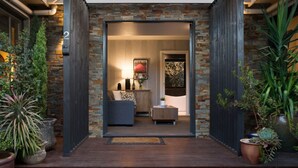 Een moderne entree van een huis met een stenen gevel, een houten terras en potplanten.