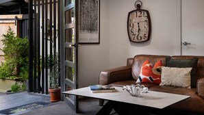 Een moderne woonkamer met een leren bank, een salontafel en een wandklok. Er is een deur met een ruit en een lijst met een afbeelding erboven.