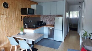 Eine kleine Küche mit Mikrowelle, Herd, Spüle und Kühlschrank. Ein Esstisch mit Stühlen und ein Topf mit Pflanze stehen bereit.