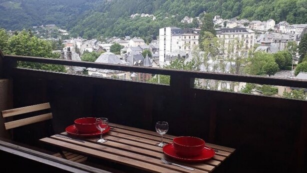 Ein Balkon mit Holztisch, gedeckt für zwei Personen, mit Blick auf eine Stadt, Gebäude und Hügel.