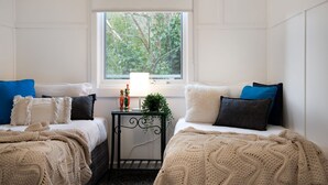 Ein Schlafzimmer mit zwei Betten, einem Fenster mit Blick ins Grüne, einem Nachttisch mit Lampe und dekorativen Gegenständen.