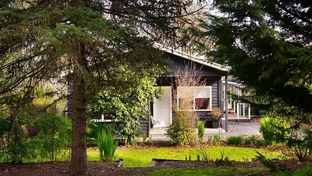 Ein modernes Haus mit einer überdachten Veranda, umgeben von üppigem Grün und Bäumen.