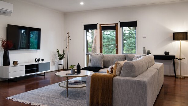 Ein modernes Wohnzimmer mit grauem Sofa, Couchtisch und flachbildfernseher an der Wand.