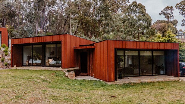 Une maison moderne à deux étages, dotée de grandes fenêtres en verre et d’une façade rouge.