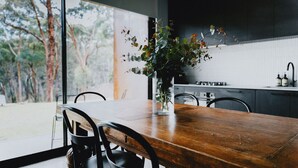 Une table à manger en bois avec des chaises, un vase avec des plantes vertes et, au fond, une cuisine.