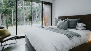 Une chambre avec un grand lit, un banc et une vue sur les arbres, visible à travers une porte vitrée.