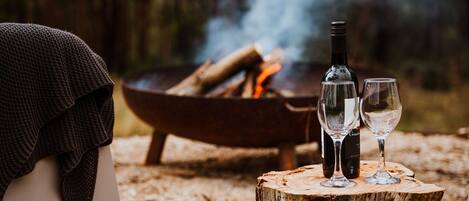A cozy outdoor setting with a fire pit, two glasses, and a bottle, suggesting a relaxed outdoor dining experience.