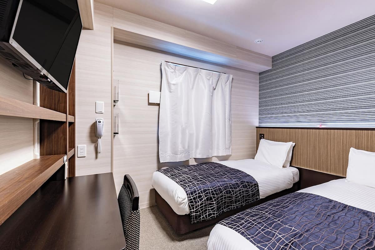 Ein Hotelzimmer mit zwei Betten, einem Schreibtisch, einem Fernseher und einem Badezimmer mit Vorhang.