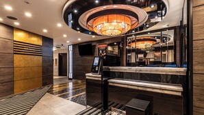 Een moderne hotel lobby met een kroonluchter, een receptiebalie en een kiosk voor digitaal inchecken.