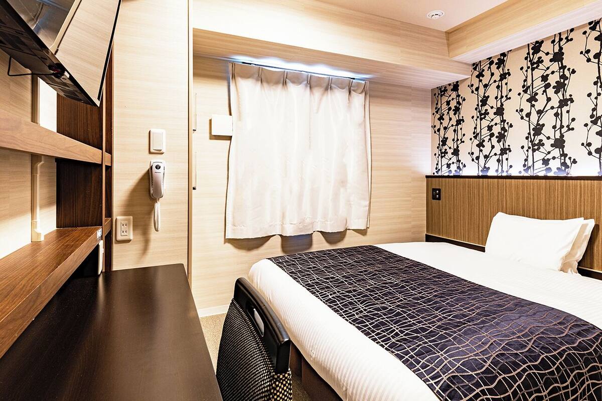 Ein Hotelzimmer mit Bett, Schreibtisch, Telefon und einem Fenster mit Vorhängen.
