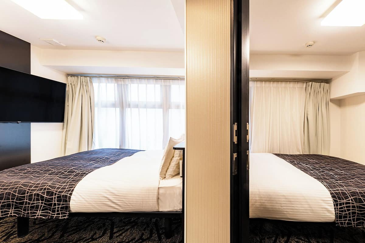 Ein Hotelzimmer mit zwei Betten, einem Flachbildfernseher und einem großen Fenster mit Vorhängen.