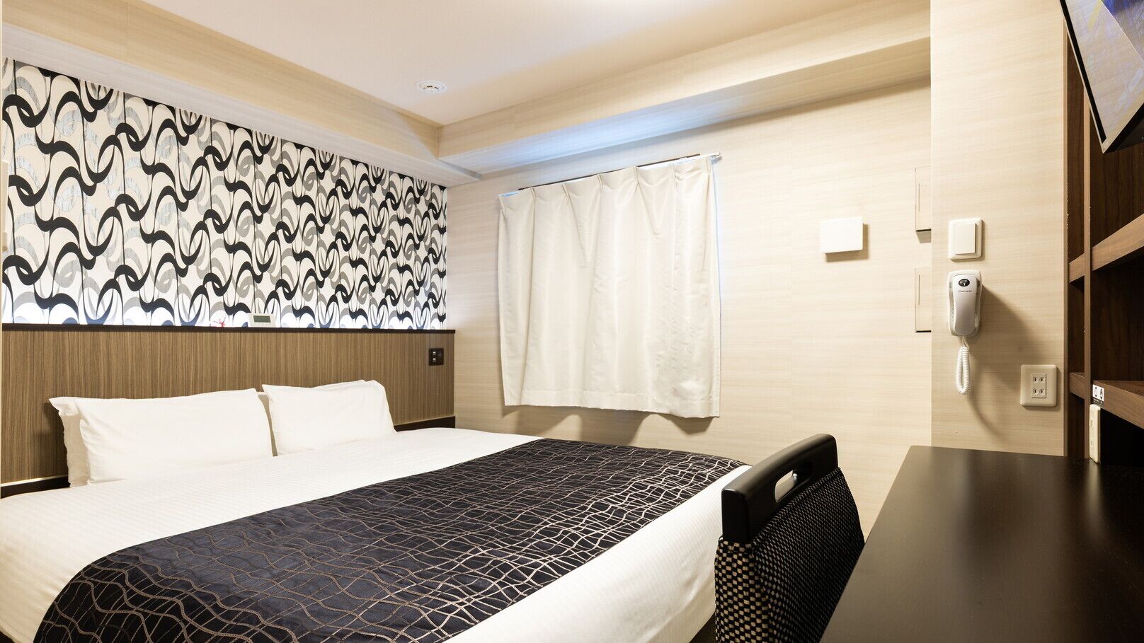 A hotel room with a bed, a desk, a telephone, and a window with curtains.