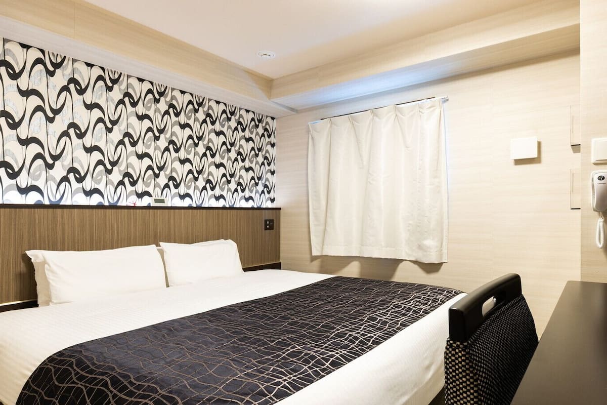 Ein Hotelzimmer mit Bett, Schreibtisch, Telefon und einem Fenster mit Vorhängen.