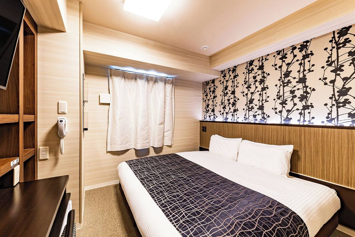 Ein Hotelzimmer mit Bett, Schreibtisch, Fernseher, Telefon und einem Fenster mit Vorhängen.