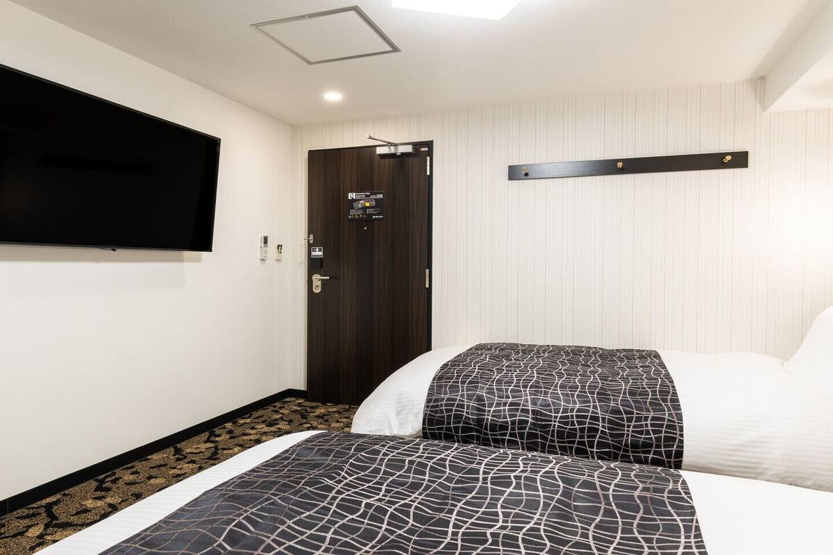 Ein Hotelzimmer mit einem Bett, einem an der Wand befestigten Fernseher, einer Tür und einer Leuchte.
