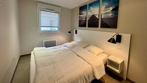 A bedroom with a bed, a nightstand, a lamp, a window, and three paintings on the wall.