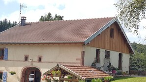 A two-story building with a red-tiled roof, a wooden extension, and a small garden area with potted plants and a bench. - Quiet & Elegant Getaway: Modern Farmhouse with Terrace, Trails & No Overlook (Le Tholy)