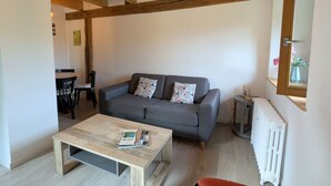 A living room with a sofa, a coffee table, a wooden ceiling, and a radiator. - Quiet & Elegant Getaway: Modern Farmhouse with Terrace, Trails & No Overlook (Le Tholy)