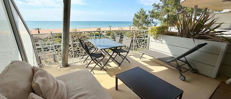 A balcony with a view of the sea, a table, chairs, and a lounge chair.