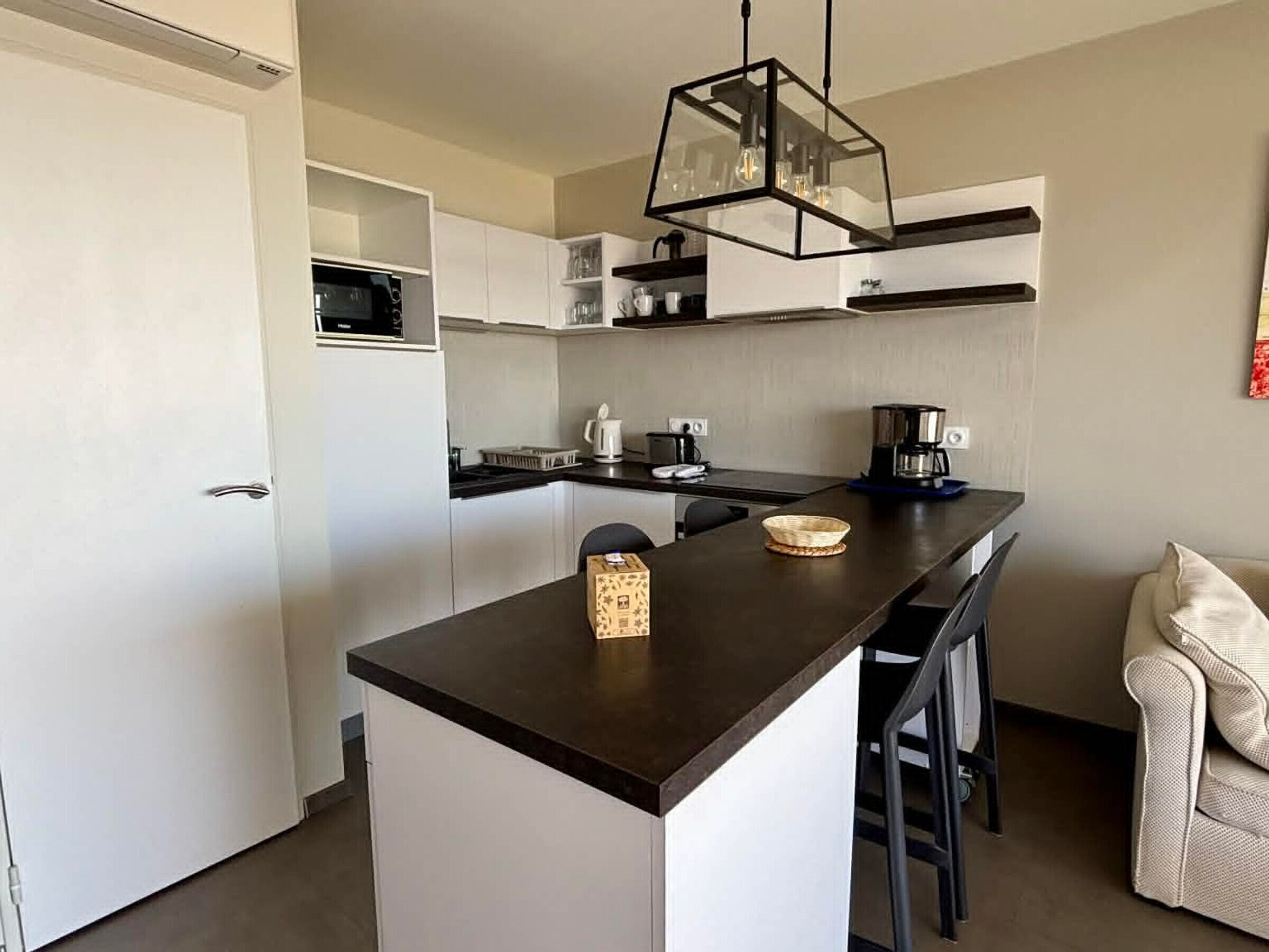 A modern kitchen with a central island, white cabinetry, and a hanging light fixture.