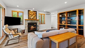 A modern living room with a fireplace, a television, and a wooden bookshelf. - Hauts-Bois Ski In/Out 2brs w/Pool Access (193-1) (Mont-Tremblant)