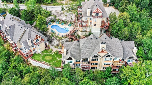 A large, multi-story house with a swimming pool surrounded by trees. - Hauts-Bois Ski In/Out 2brs w/Pool Access (193-1) (Mont-Tremblant)