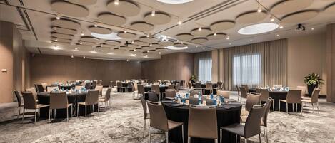 A conference room with multiple tables, chairs, and a high ceiling with circular lighting fixtures.