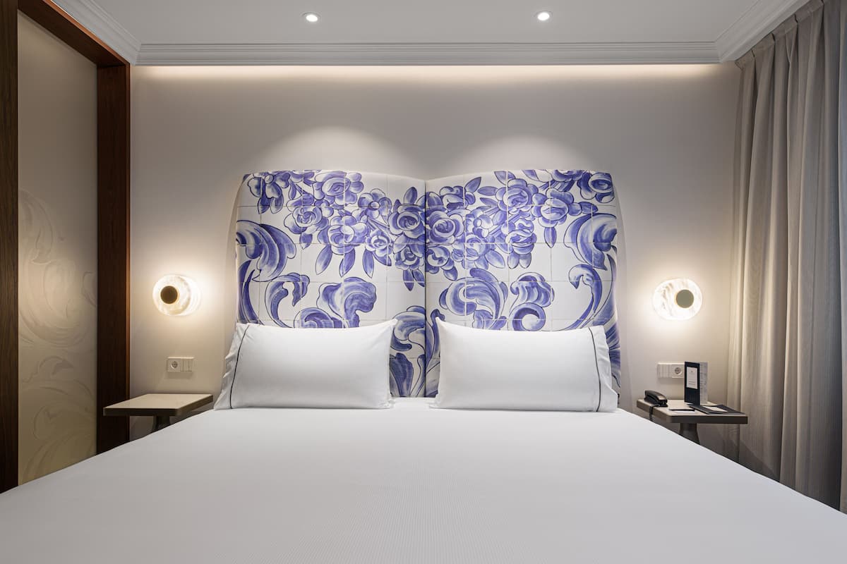 Ein Hotelzimmer mit einem großen Bett, zwei Nachttischen und einer Wand mit floralem Muster.