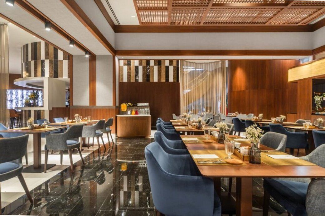A modern hotel lobby with a long reception desk, multiple seating areas, and a decorative wall with vertical elements.