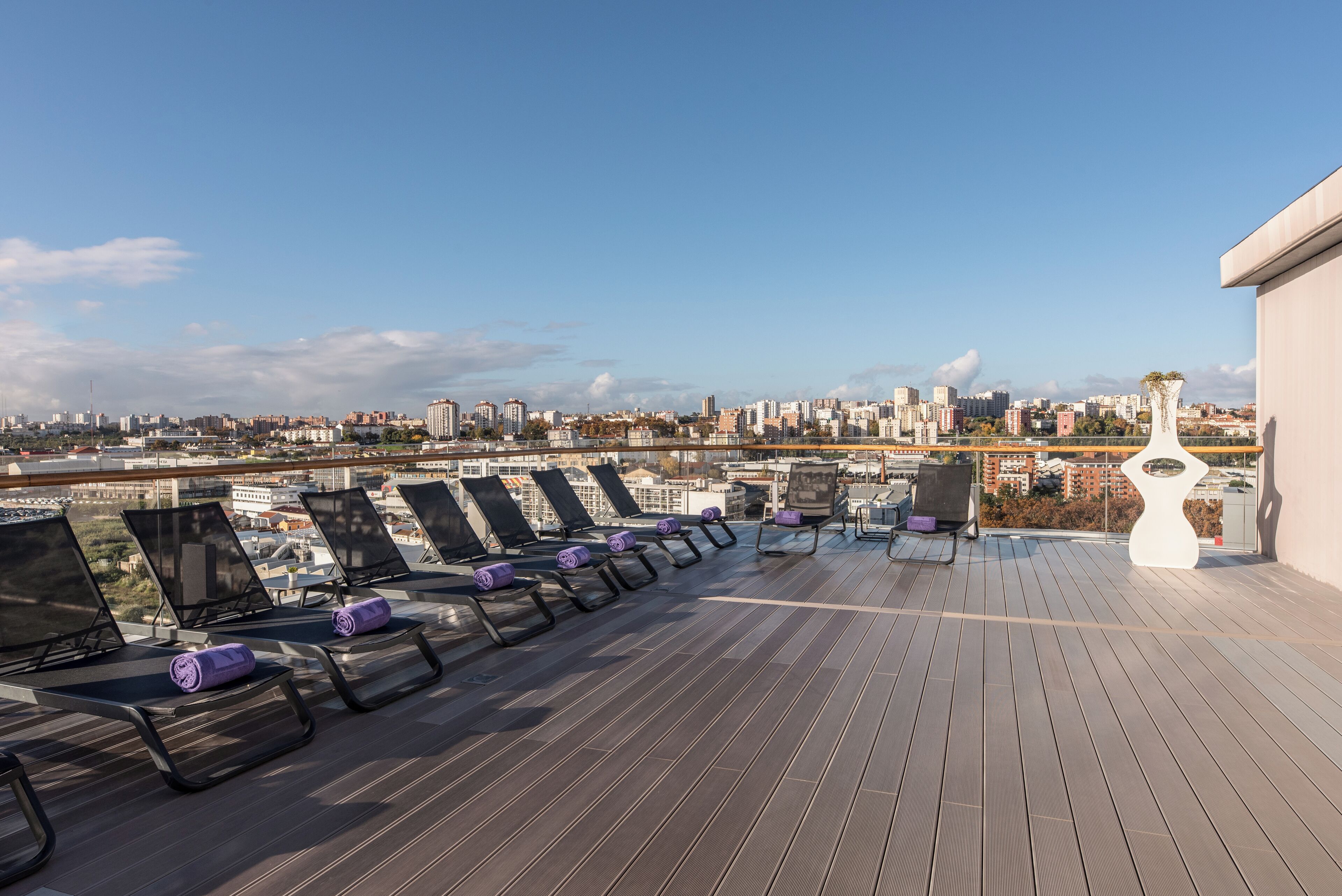 A rooftop terrace with sun loungers and a view of a cityscape.