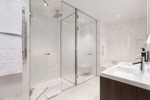 A modern bathroom with a glass-enclosed shower, a wooden vanity, and marble flooring.